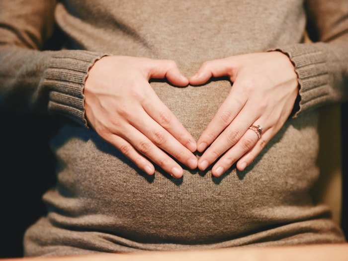 Hands forming a heart shape over a pregnant belly — prenatal, postpartum, and women's health nutrition